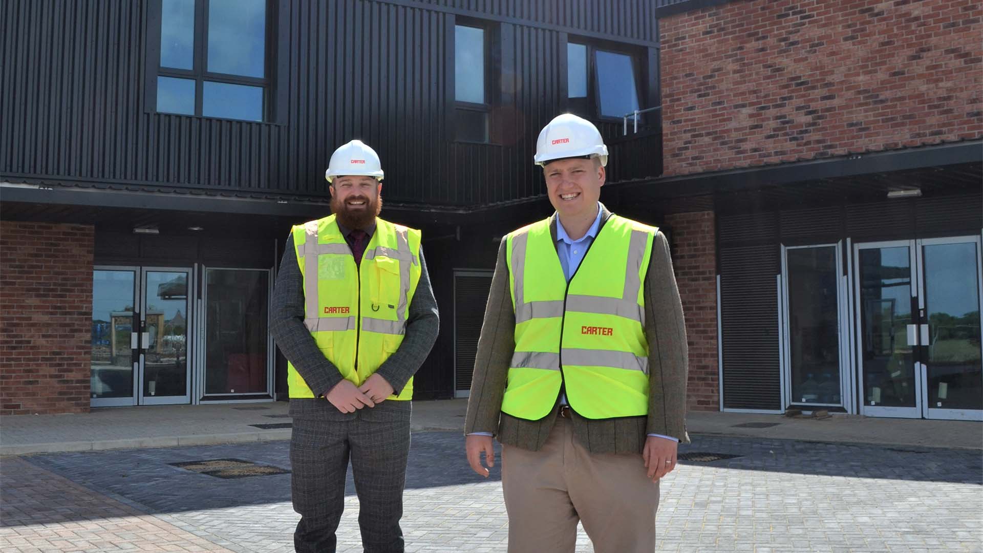 Two men in high visibility jackets looking at the camera, standing in front of a new office.