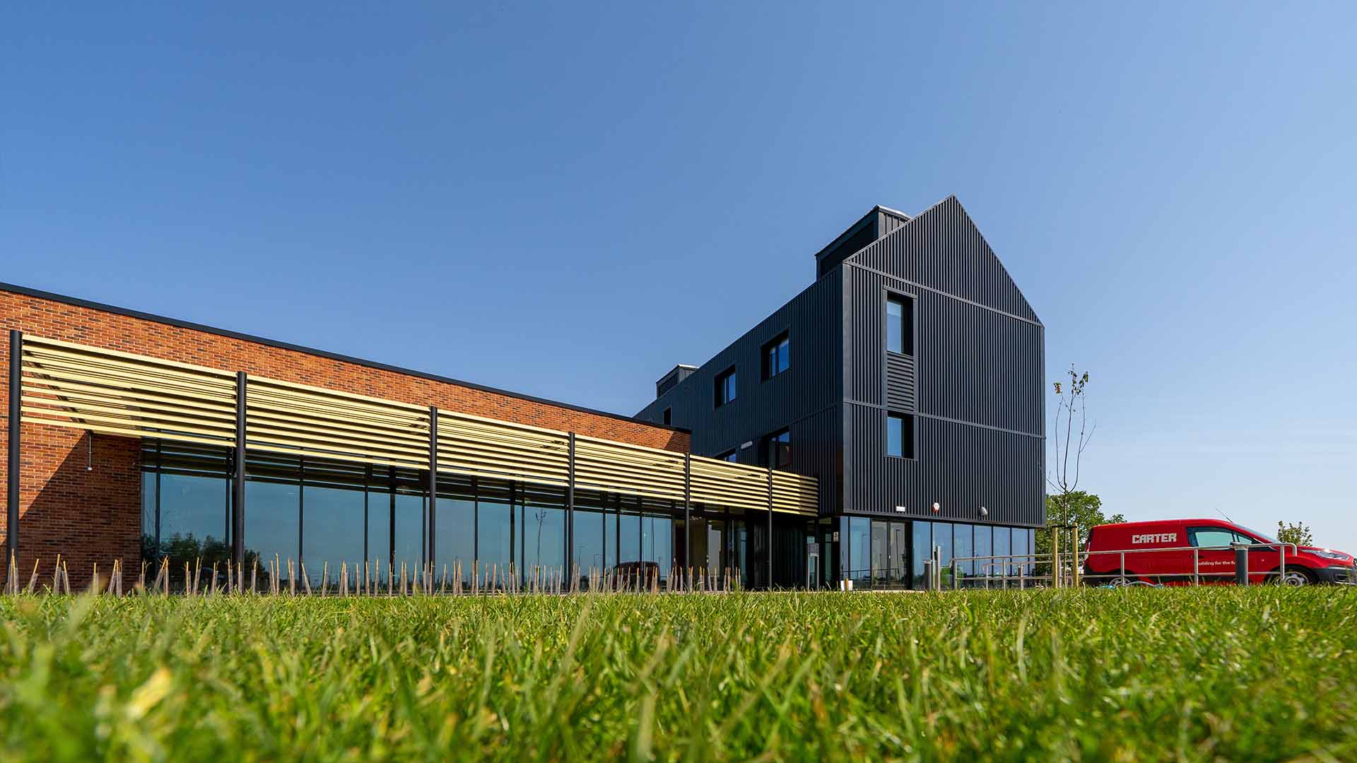 A low shot of a new office space set against a clear, blue sky. The main building is composed of dark wood and modern glass.